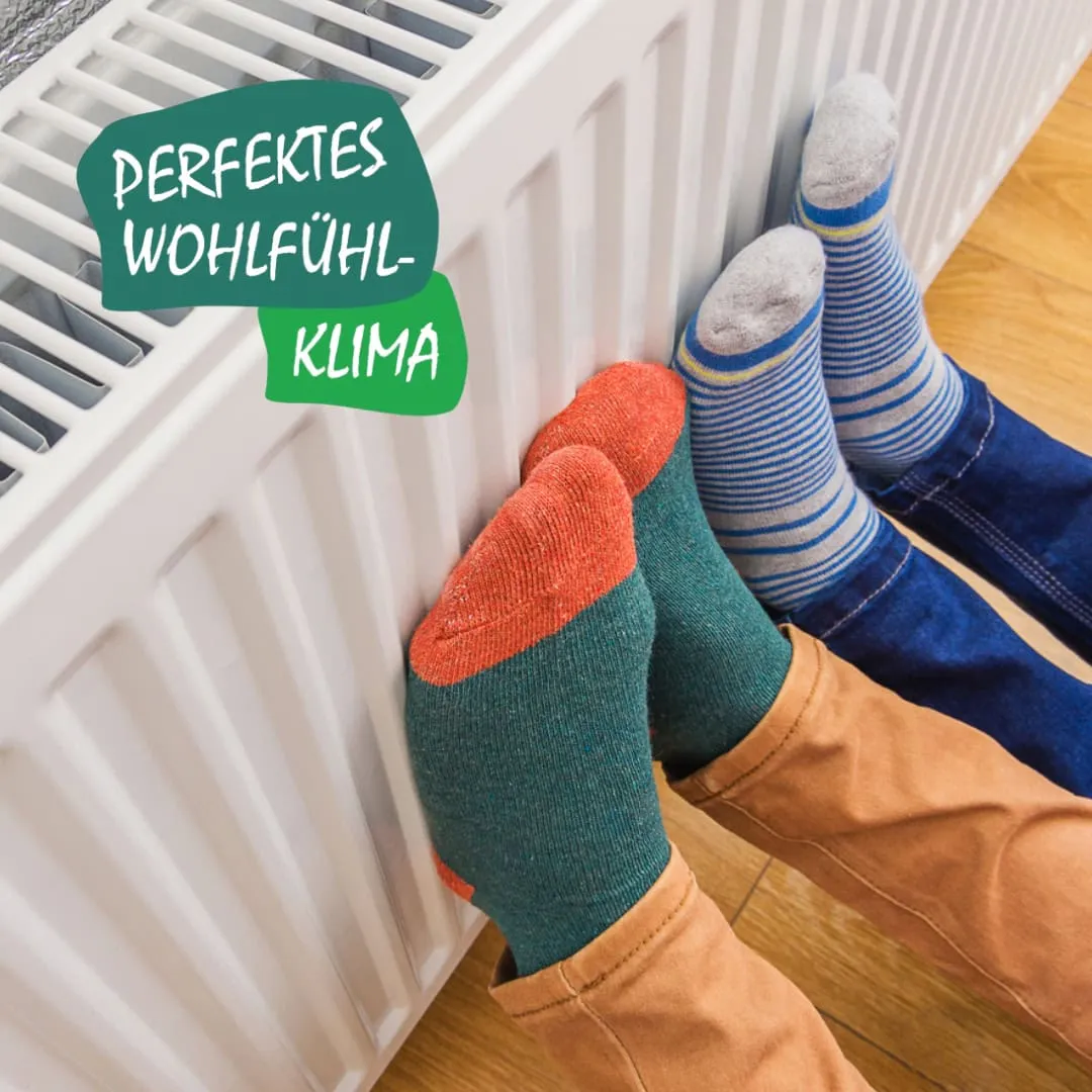 Zwei junge Menschen strecken ihre Füße an die warme Heizung. Slogan: Perfektes Wohlfühlklima.